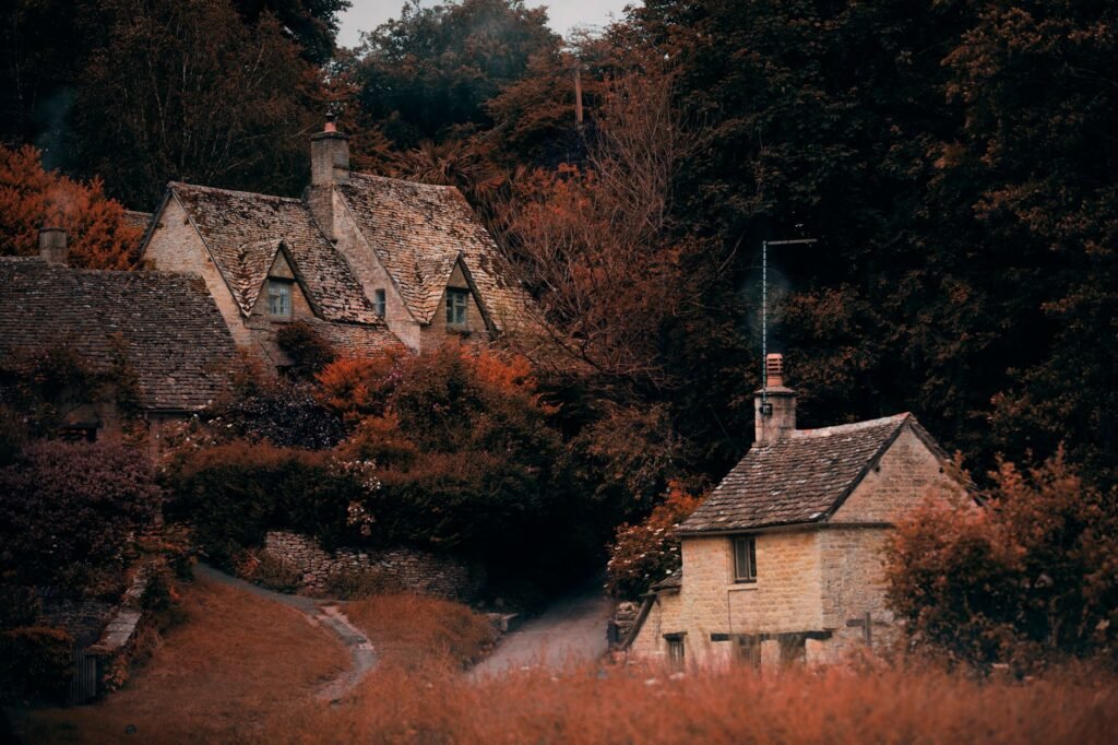 Quaint stone cottages surrounded by vibrant autumn foliage in Bibury, England.