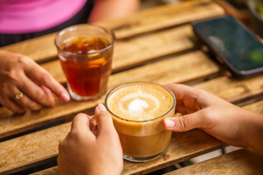 Two people enjoying coffee on a wooden table outdoors. Captured during the day with a warm and inviting atmosphere.