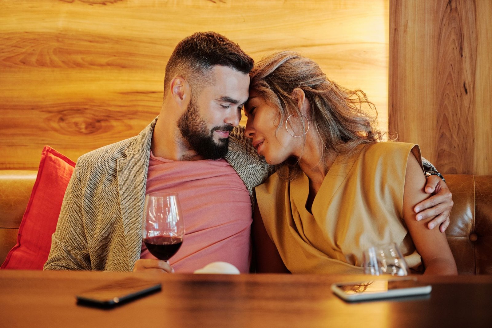 A couple shares an intimate moment with wine glasses at a cozy restaurant setting.