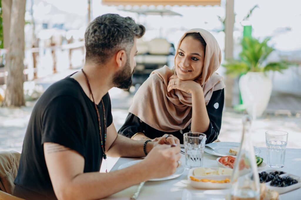 A couple enjoying a romantic lunch together outdoors, seated and smiling warmly.