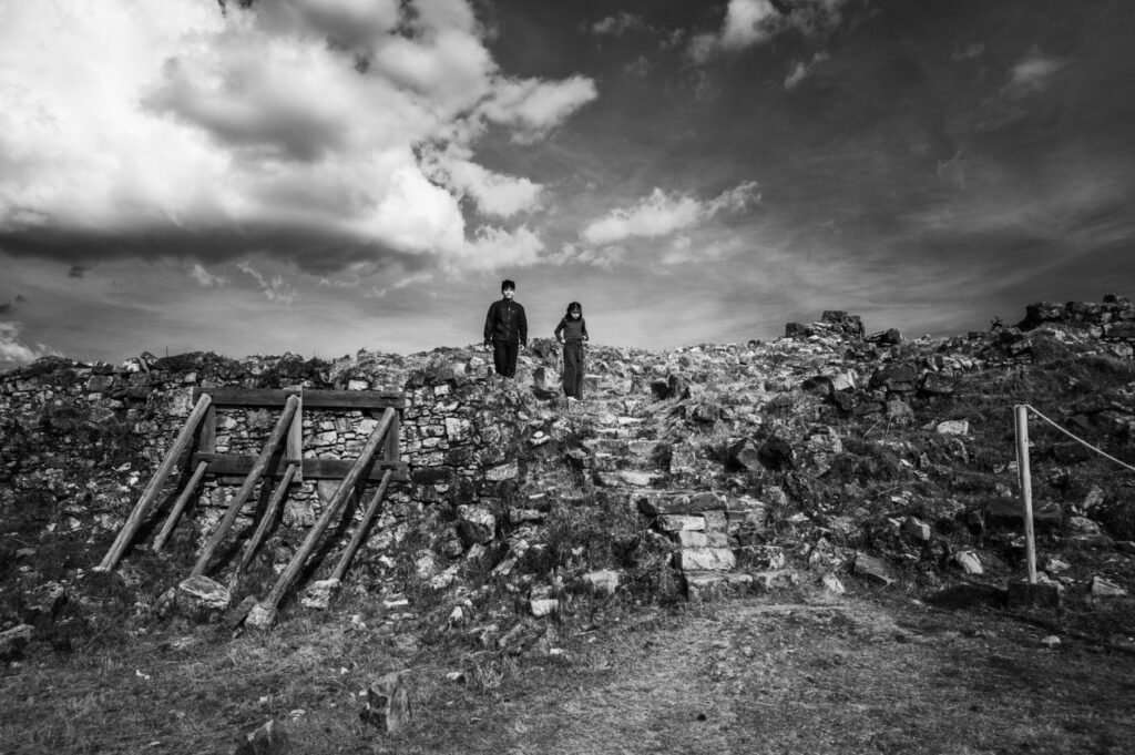 A black and white photo of two people walking through ancient ruins in Huamachuco, Peru.