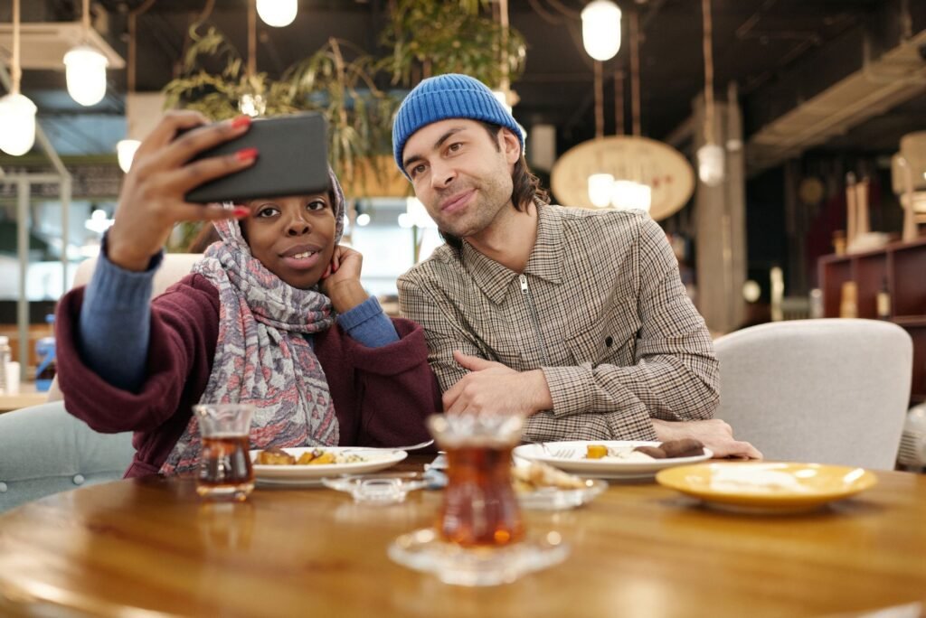 A cheerful interracial couple capturing a selfie while enjoying a meal in a modern cafe.