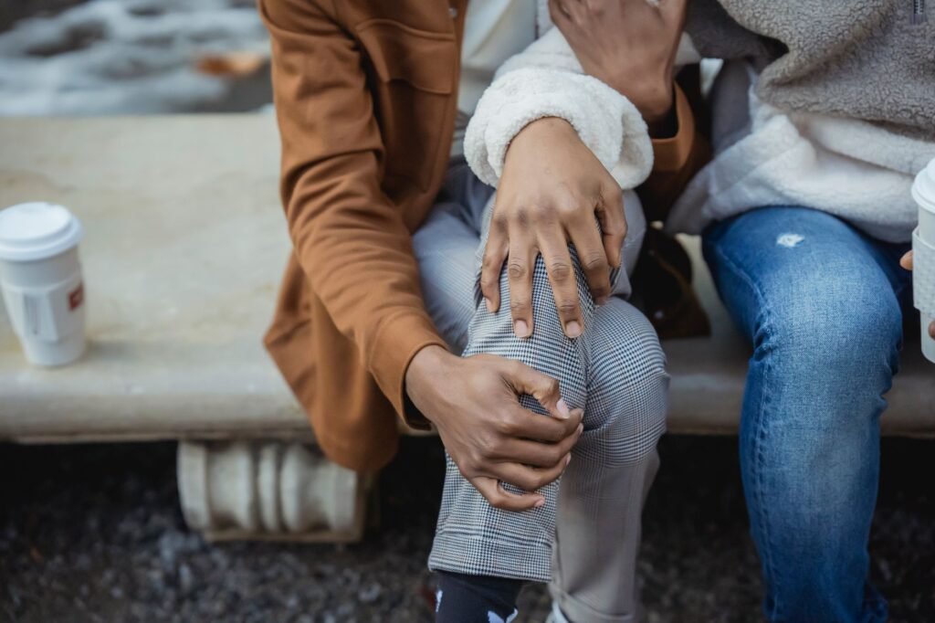 Unrecognizable African American person hugging faceless partner while sitting on bench with takeaway coffee during date on st