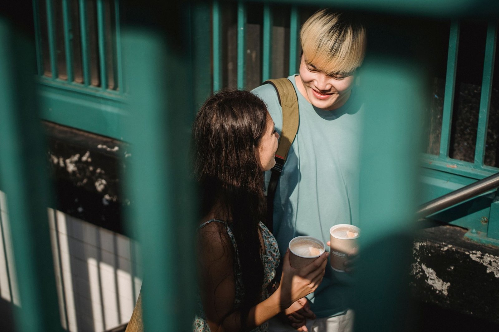 Cheerful glad multiracial couple with cups of coffee looking at each other and going up stairs with metal railing