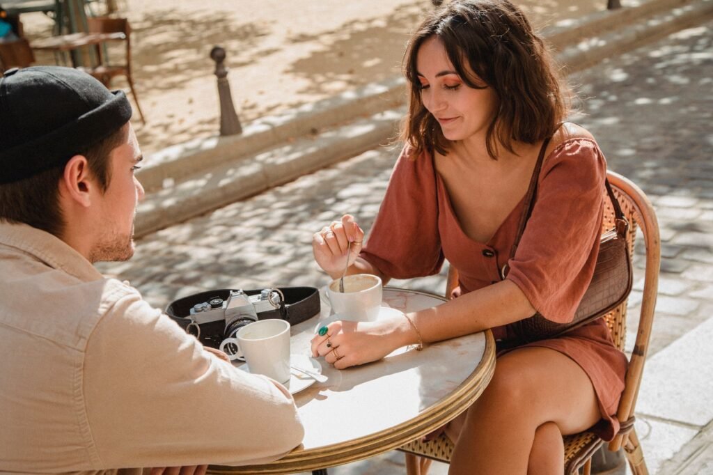 Couple enjoying coffee and conversation at an outdoor café on a sunny day.