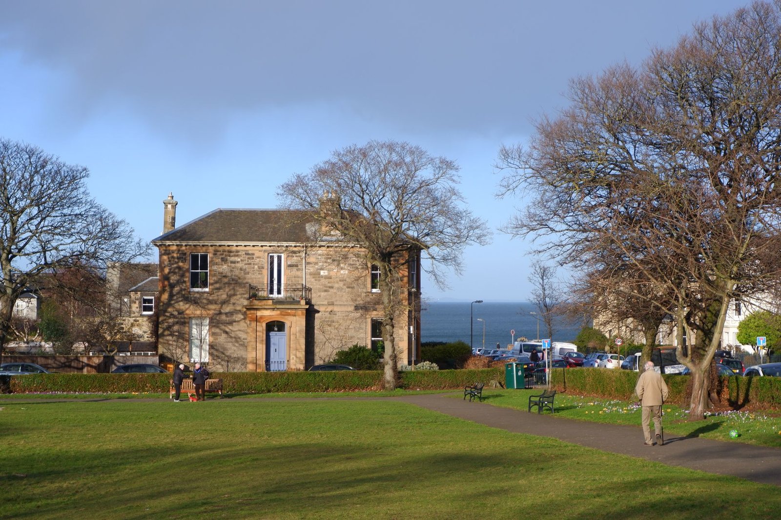 A quaint park in Edinburgh featuring a historic stone house, path, and sea view.