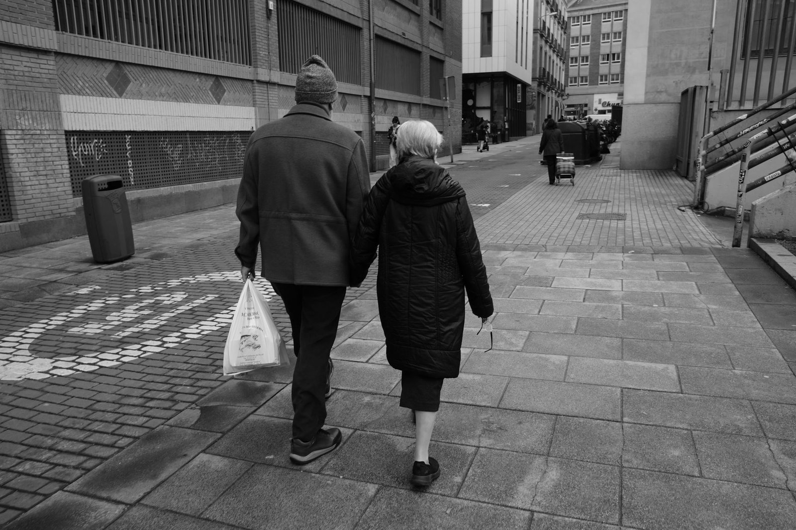 A senior couple walks through an urban street, creating a touching city moment.