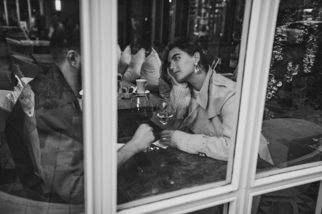 Black and white image of a couple enjoying a romantic date with wine by a window.