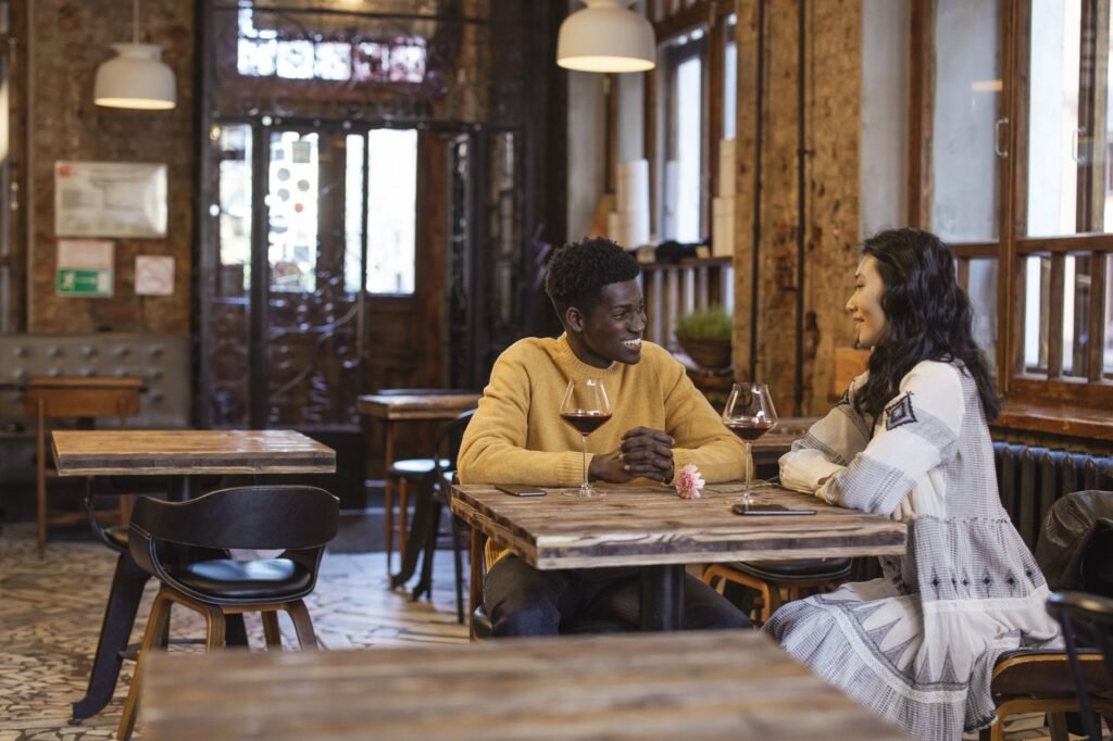 A happy interracial couple enjoys a date at a cozy cafe, sharing smiles and wine.