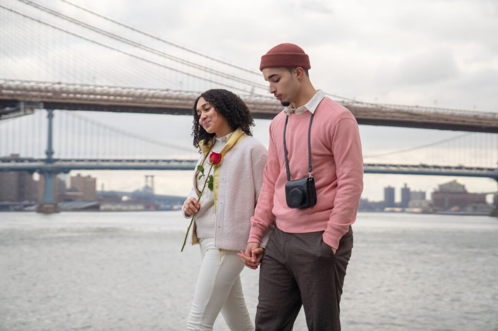 Side view of tender Hispanic couple holding hands while strolling on embankment near sea against bridge during romantic date