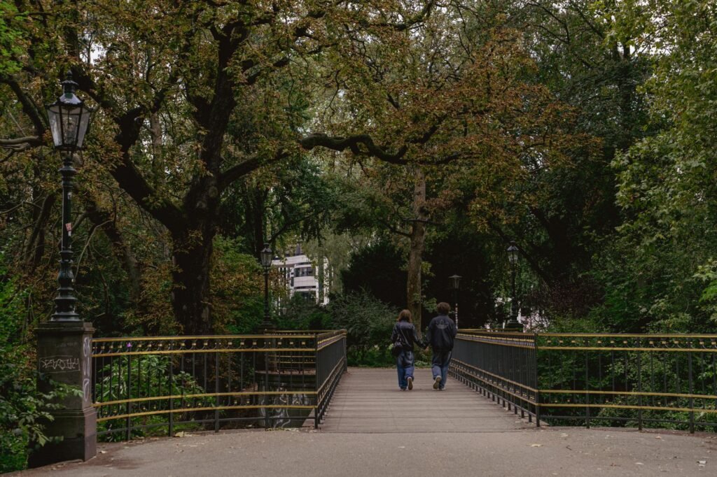 A couple walks hand-in-hand down a scenic park bridge surrounded by lush greenery.