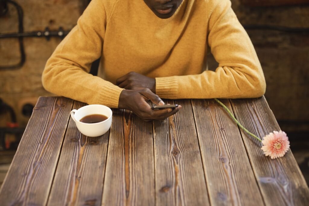 A man in a café using a smartphone with a coffee cup on a wooden table.