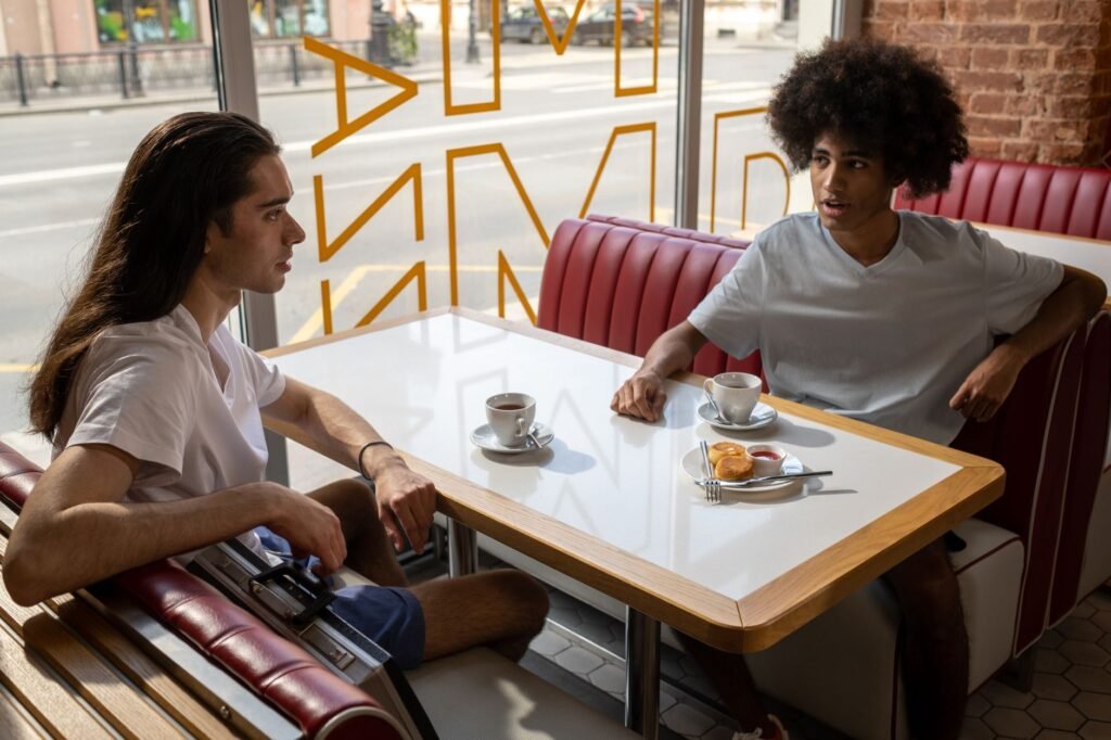 Two friends engage in conversation over coffee and pastries in a stylish café setting.