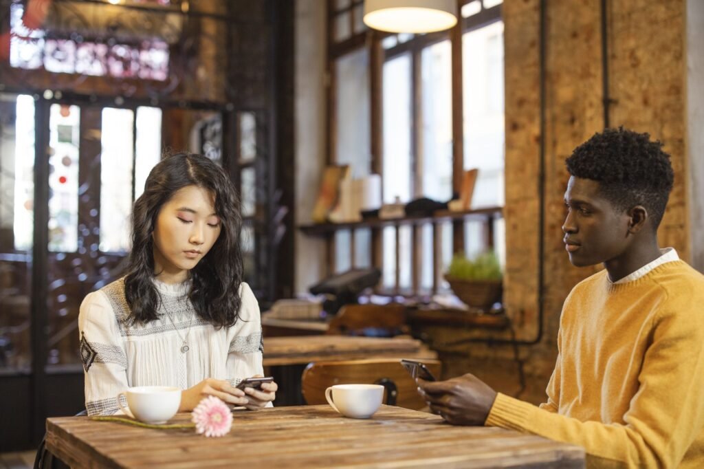 Young interracial couple in a cafe, using phones on a date. Warm setting with a rustic interior.