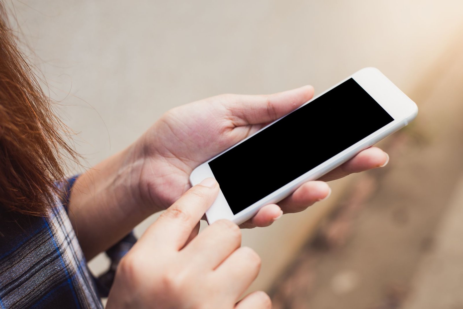Person holding and using a smartphone outdoors, focusing on hands and screen.