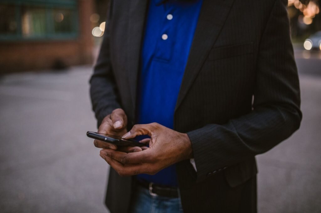 A man in a black suit using a smartphone while standing outdoors during the day.