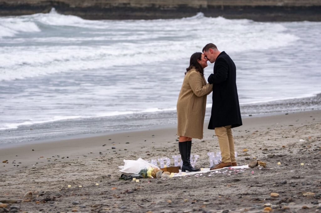 A couple in winter coats embraces during a proposal at Narragansett Beach, Rhode Island.