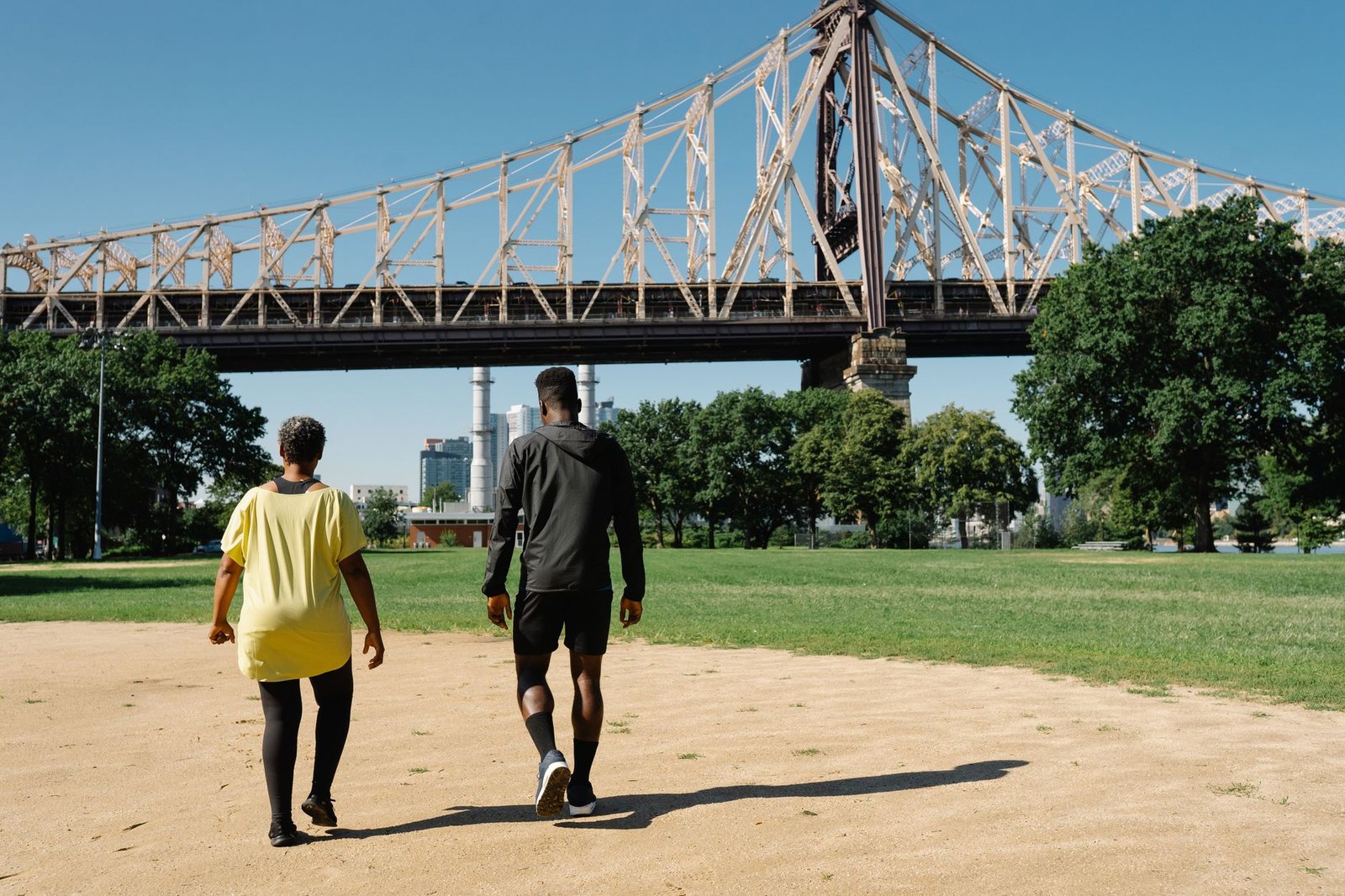 A couple enjoys a walk under a famous steel bridge in a green park on a sunny day.