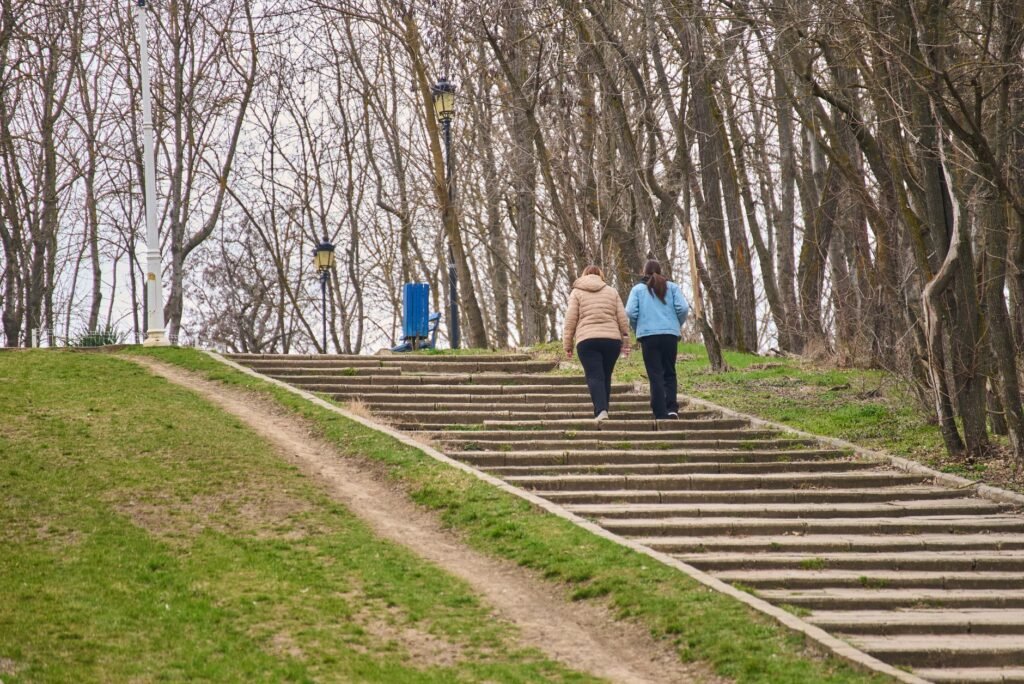 Two women enjoy a leisurely walk up a staircase in a tree-lined park path, capturing the essence of early spring.