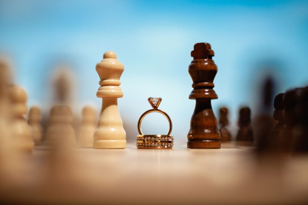 Creative shot of gold wedding rings between chess pieces outdoors against a clear blue sky.