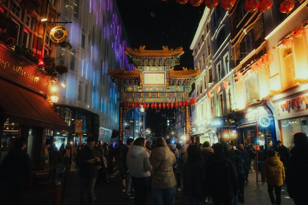 Bustling evening in London's Chinatown with illuminated Chinese gate and lively crowd.