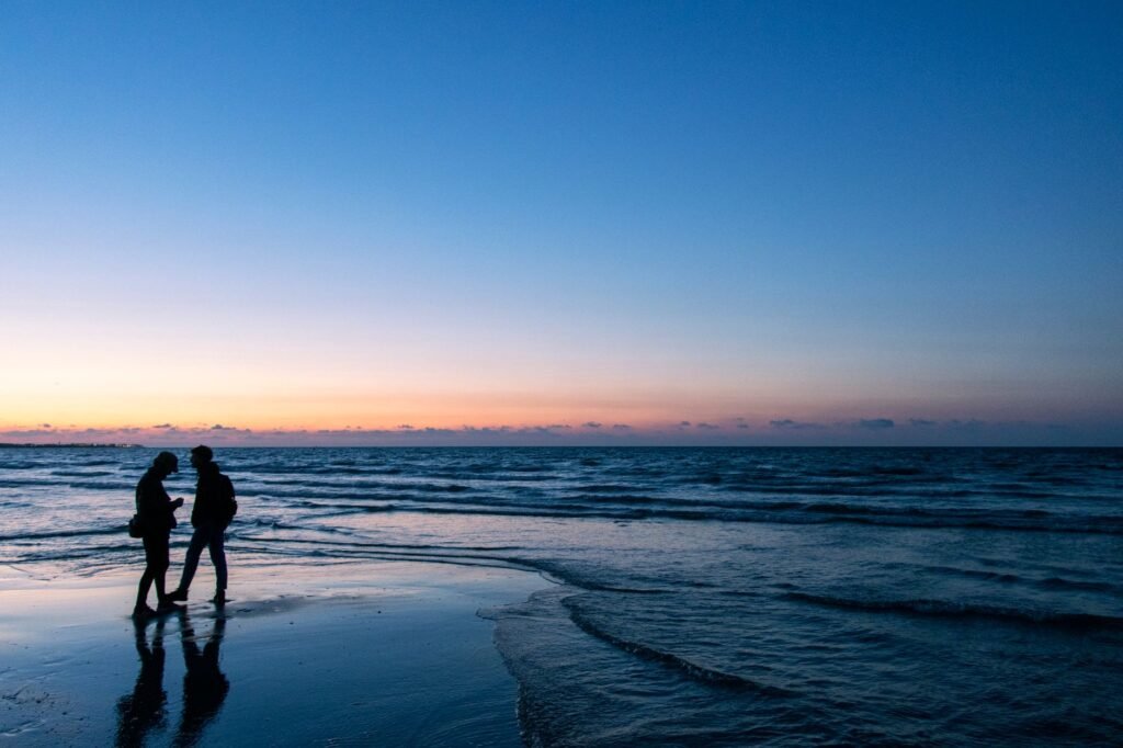 A silhouetted couple walks along the Dieppe beach in Normandy, France, during a serene sunset.