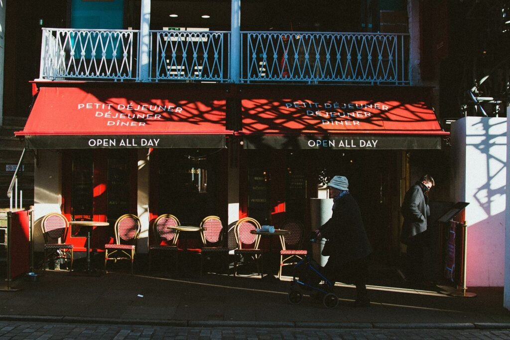 Sunlit outdoor cafe with pedestrians walking by, creating a lively street atmosphere.