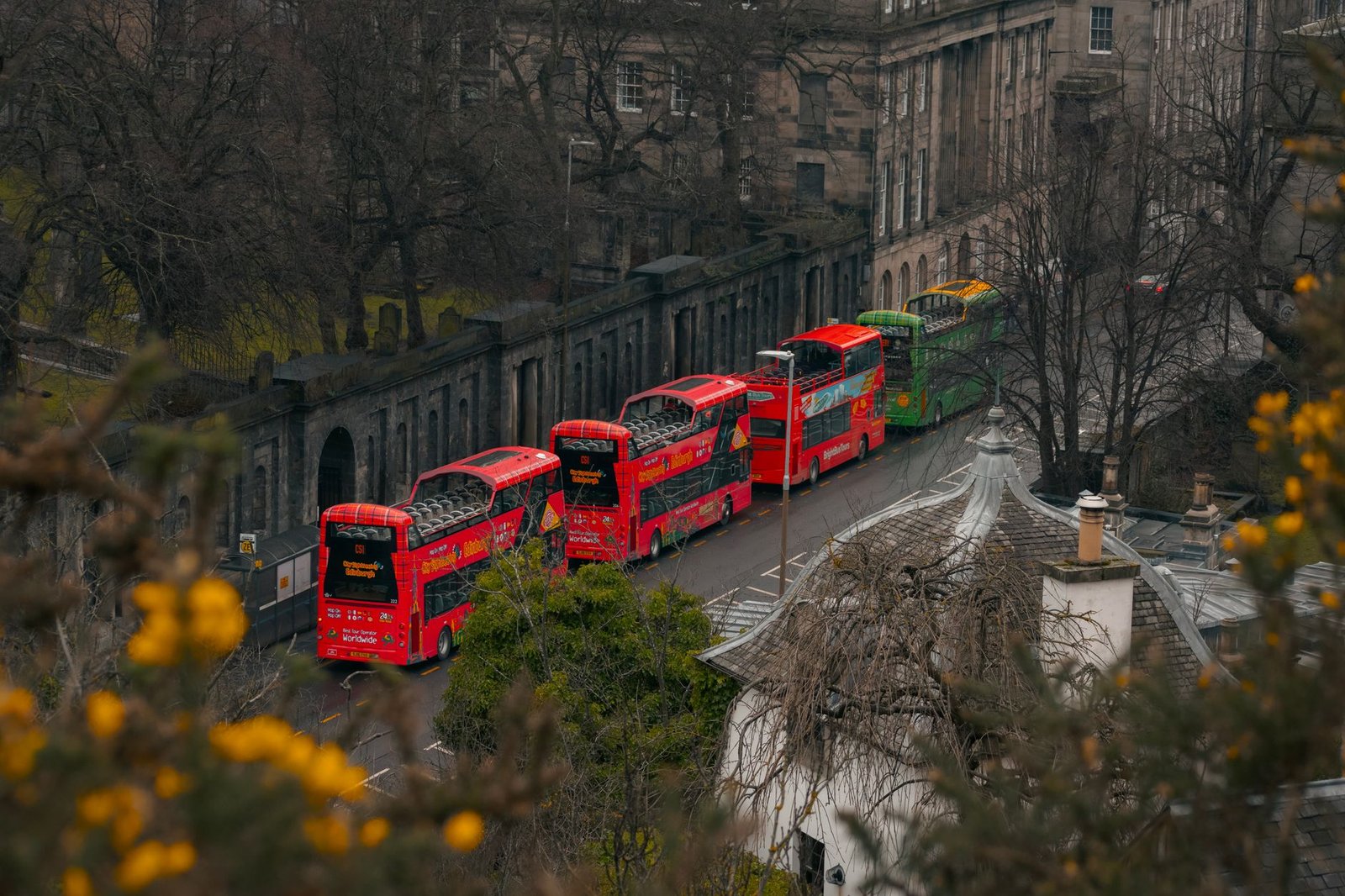 Vibrant double decker buses navigate an Edinburgh street, highlighting urban traffic.