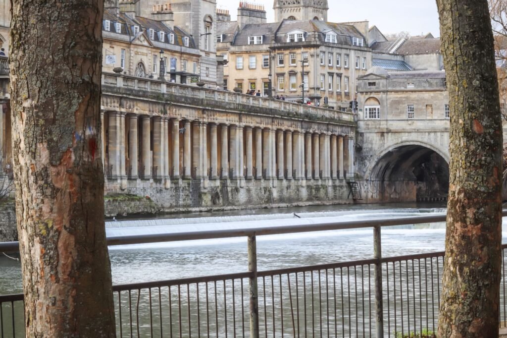 Elegant architectural buildings along a river in a historic European city, framed by trees.