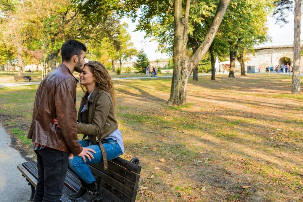 A loving couple enjoys a tender moment on a park bench surrounded by autumn trees.