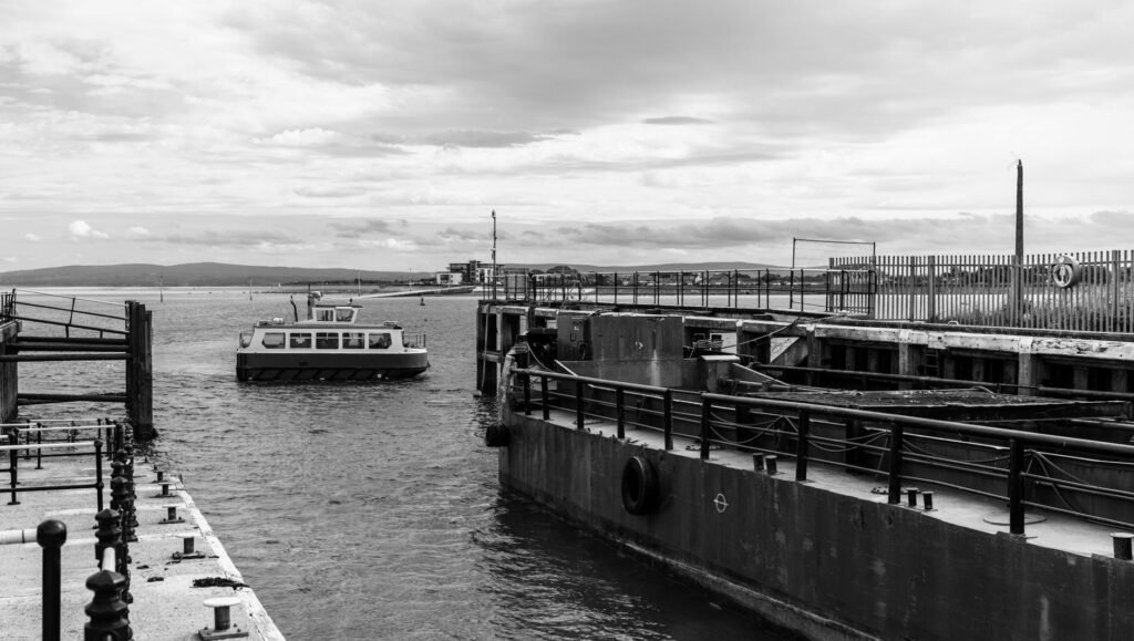Calm scene of a ferry at Blackpool dock in monochrome, highlighting industrial structures and calm waters.