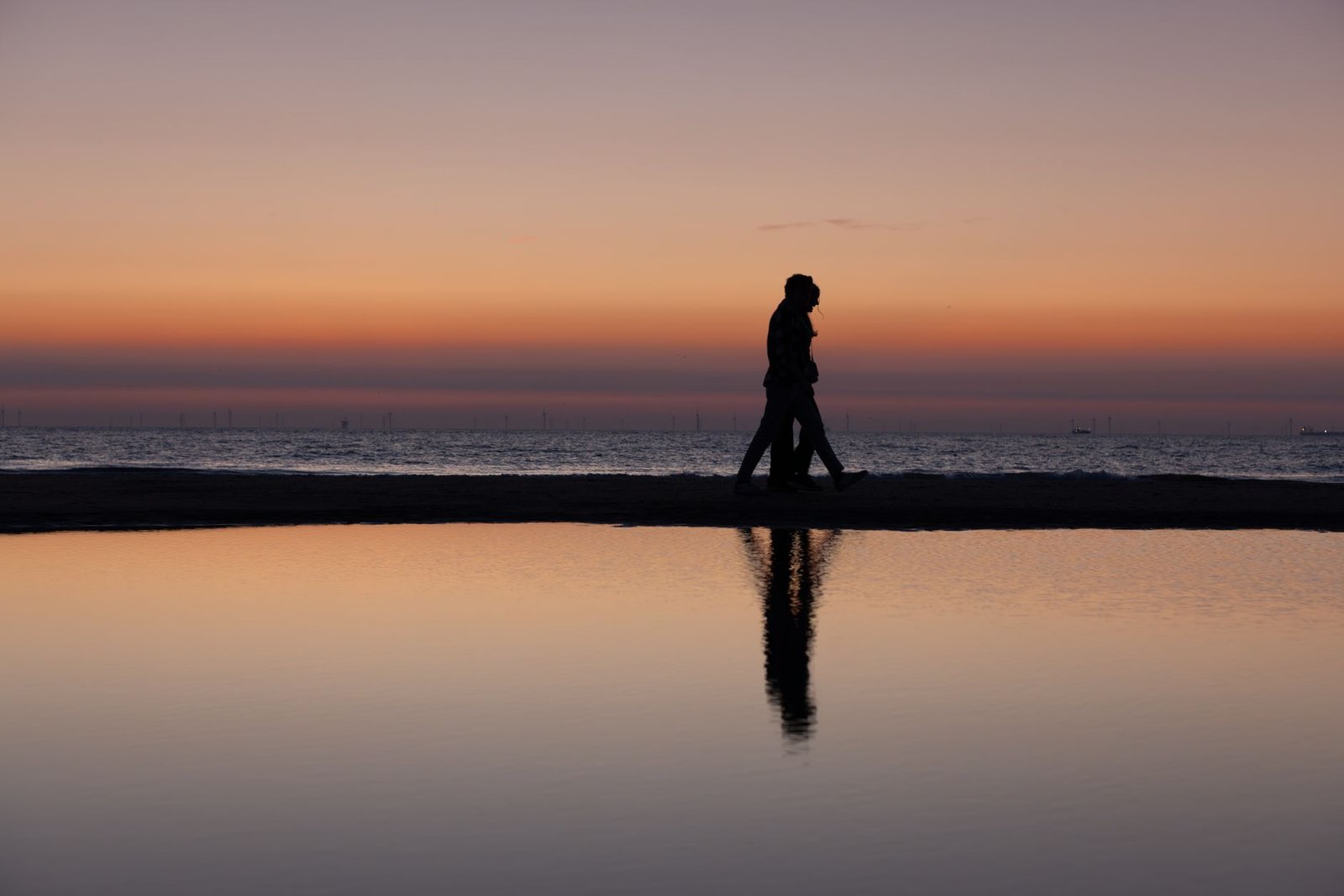 Silhouette of a couple walking along the beach during a serene sunset with calm reflections.