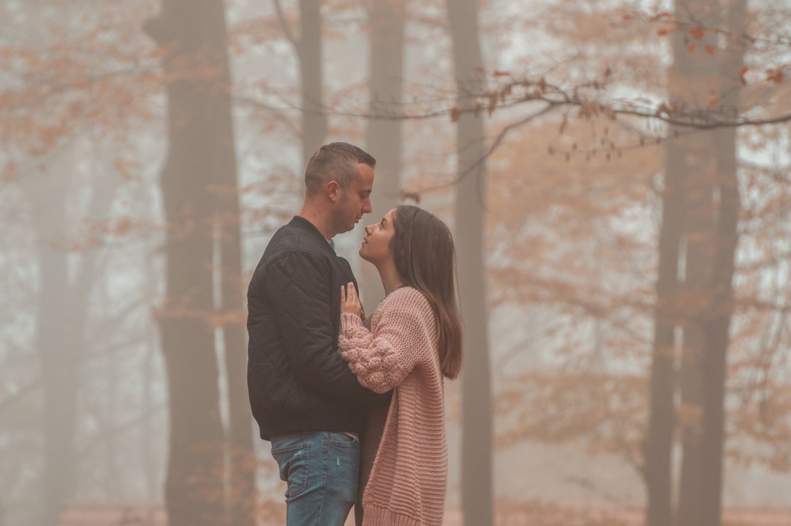 A loving couple embraces in a misty forest during autumn, creating a serene and romantic mood.
