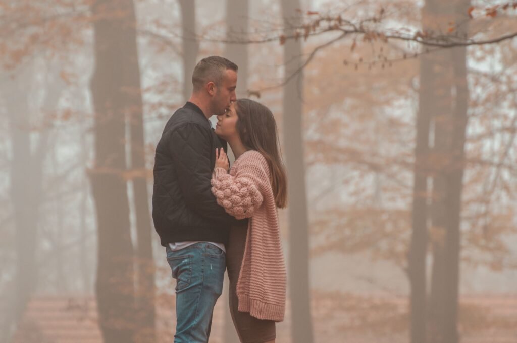 A couple sharing a tender moment in a foggy autumn forest, evoking romance and tranquility.