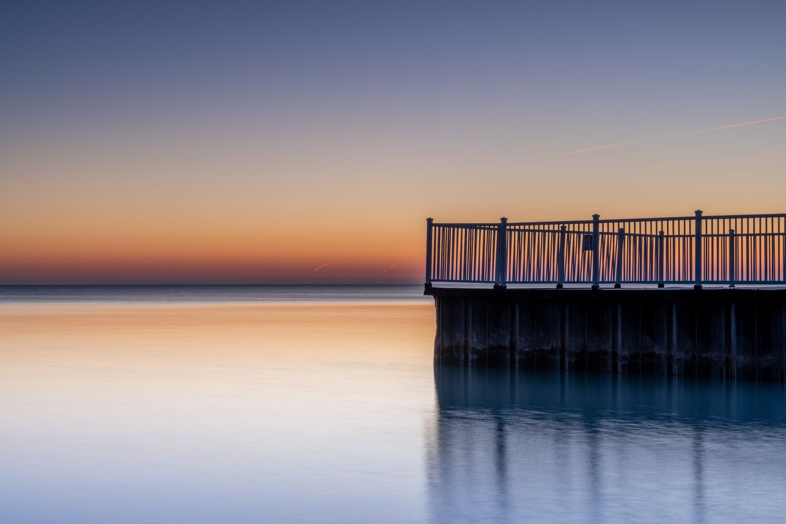 Big wooden dock built near tranquil endless sea under orange and blue sky in picturesque evening