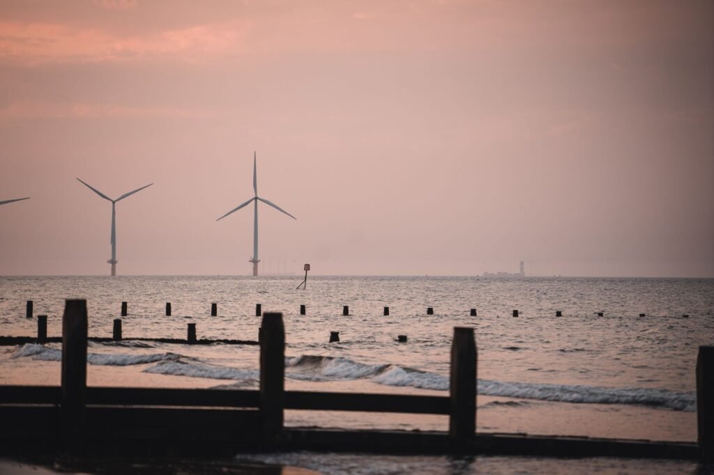 Wind turbines at sea during a serene sunset in York, England. Calm waves and pastel hues create a tranquil scene.